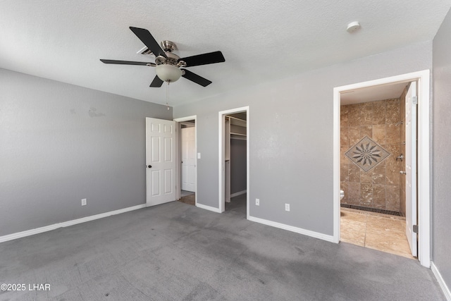 unfurnished bedroom with a closet, ensuite bathroom, a ceiling fan, carpet floors, and a walk in closet