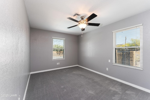 spare room with baseboards, dark colored carpet, a ceiling fan, and visible vents