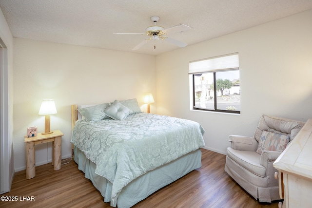 bedroom with a ceiling fan, a textured ceiling, baseboards, and wood finished floors