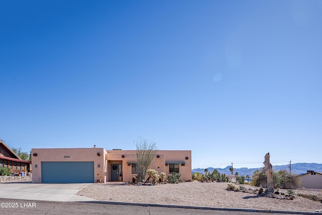 pueblo-style house featuring a mountain view, driveway, an attached garage, and stucco siding