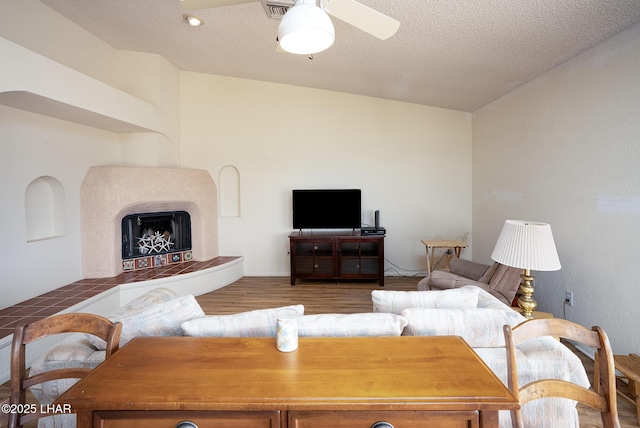 living area featuring a fireplace with raised hearth, ceiling fan, a textured ceiling, wood finished floors, and visible vents