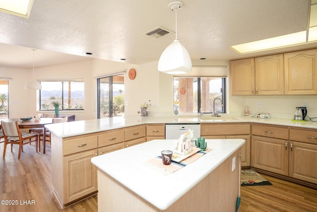 kitchen with light brown cabinetry, white dishwasher, and a sink