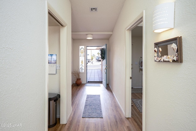 doorway featuring baseboards, visible vents, wood finished floors, and a textured wall