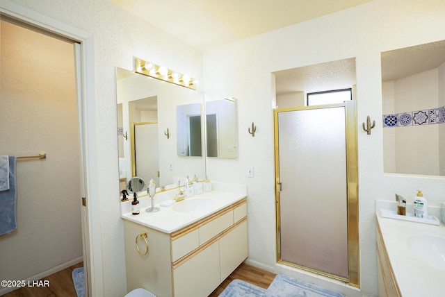 bathroom featuring baseboards, two vanities, wood finished floors, a shower stall, and a sink