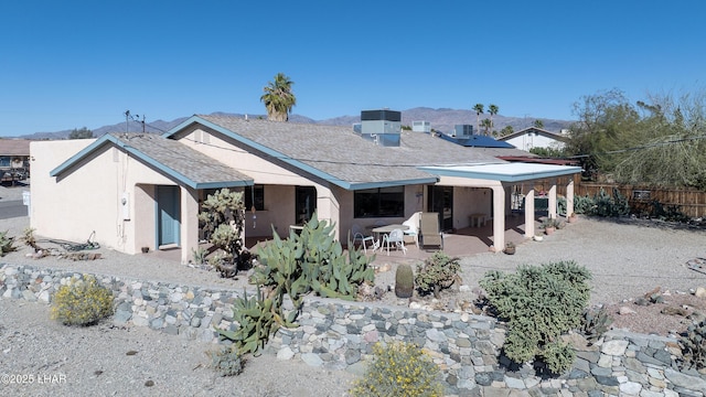 rear view of house with a shingled roof, a patio, fence, and stucco siding