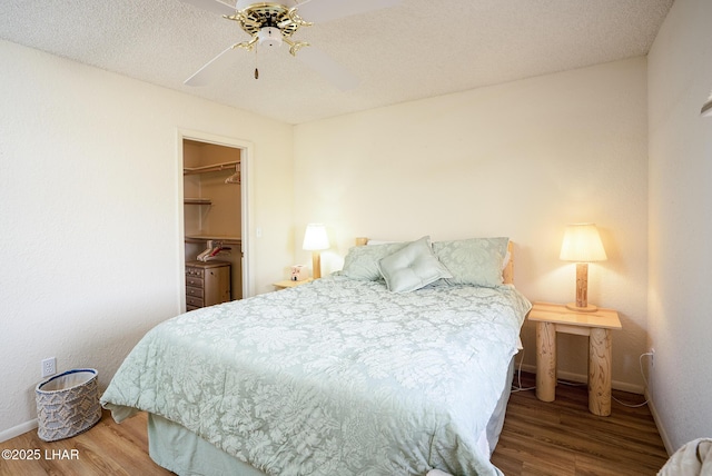 bedroom with ceiling fan, a spacious closet, wood finished floors, and baseboards