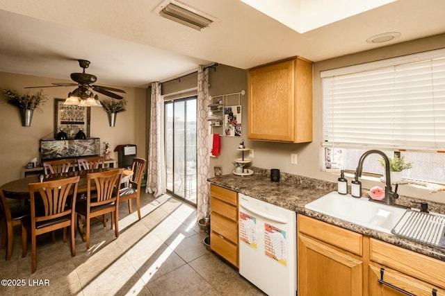 kitchen with sink, light tile patterned floors, ceiling fan, dark stone countertops, and white dishwasher