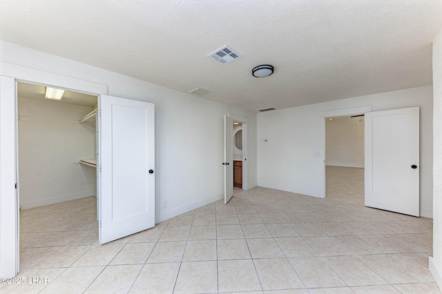 unfurnished bedroom featuring a spacious closet, light tile patterned floors, a textured ceiling, and a closet