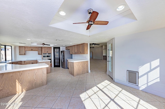 kitchen featuring appliances with stainless steel finishes, light tile patterned floors, kitchen peninsula, a raised ceiling, and a textured ceiling