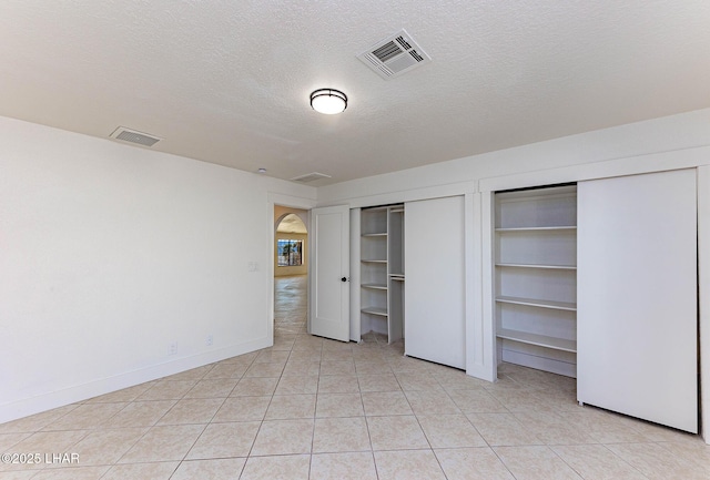 unfurnished bedroom featuring light tile patterned floors, a textured ceiling, and two closets