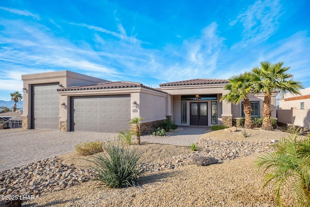 view of front facade featuring a tiled roof, decorative driveway, an attached garage, and stucco siding