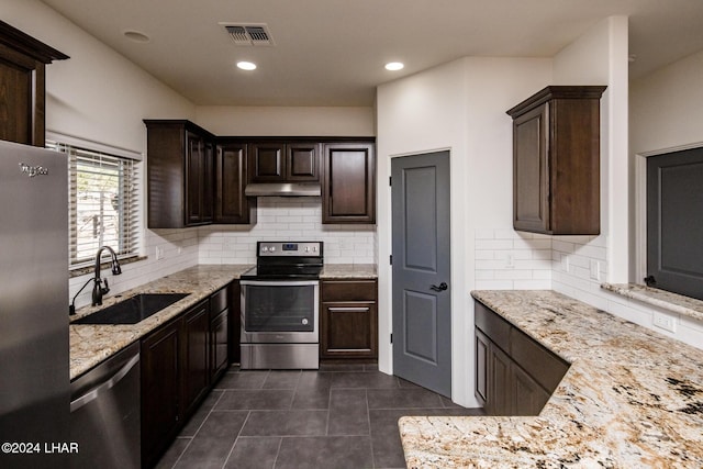 kitchen with appliances with stainless steel finishes, sink, backsplash, dark tile patterned floors, and light stone countertops