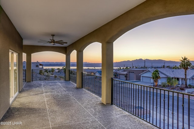 patio terrace at dusk featuring a mountain view, a ceiling fan, and a balcony