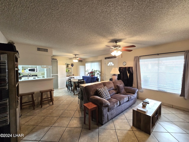 tiled living room featuring ceiling fan, a textured ceiling, and a healthy amount of sunlight