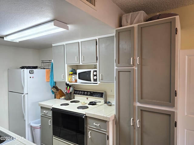 kitchen featuring white appliances, tile countertops, a textured ceiling, and gray cabinetry