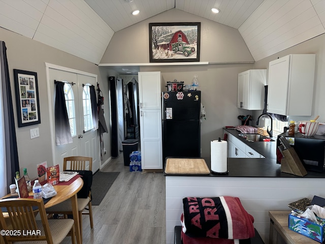 kitchen featuring dark countertops, light wood-style flooring, freestanding refrigerator, white cabinets, and a sink