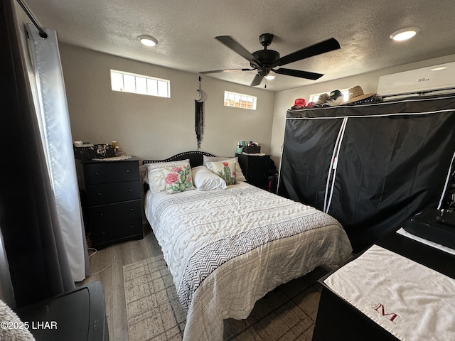 bedroom with a textured ceiling, ceiling fan, a wall unit AC, and wood finished floors