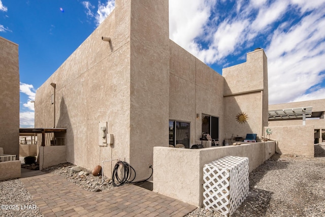 view of side of home featuring stucco siding, a patio, and a chimney