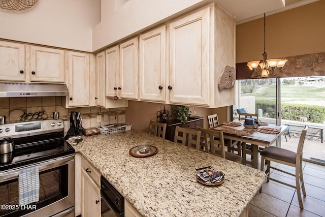 kitchen featuring under cabinet range hood, backsplash, stainless steel electric range oven, light stone countertops, and a chandelier