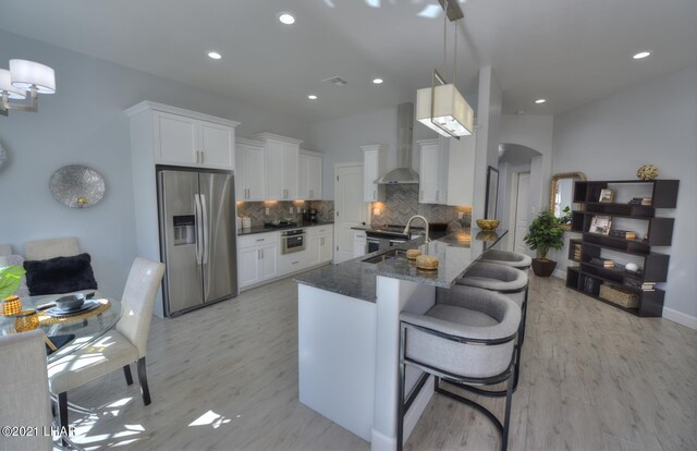8551 River View Villas Dr Unit 15, Parker, AZ 85344 - kitchen with stainless steel refrigerator with ice dispenser, wall chimney range hood, arched walkways, decorative backsplash, and dark stone counters