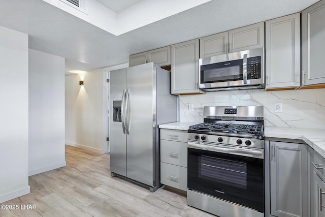 kitchen featuring baseboards, appliances with stainless steel finishes, light wood-type flooring, gray cabinets, and decorative backsplash