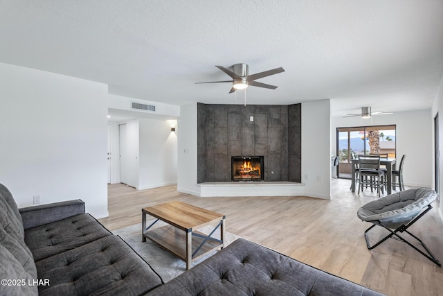 living room featuring a textured ceiling, light wood-style flooring, a fireplace, and visible vents