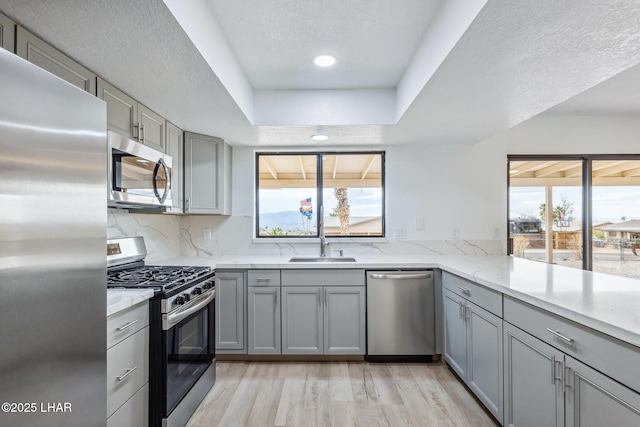 kitchen featuring light stone counters, light wood-style flooring, gray cabinetry, stainless steel appliances, and backsplash