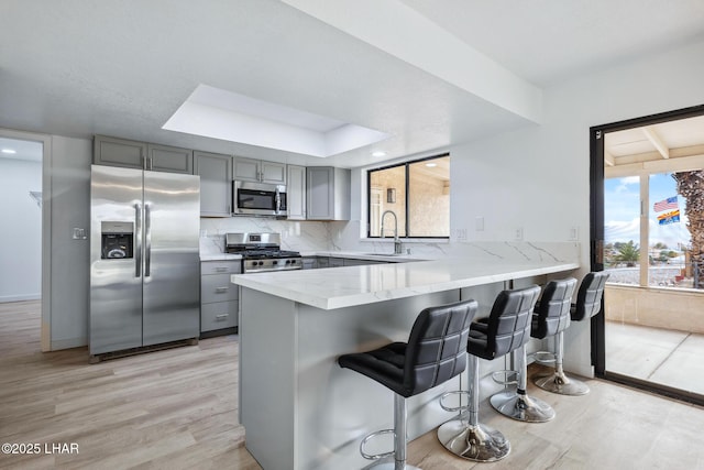 kitchen featuring light stone counters, light wood-style flooring, appliances with stainless steel finishes, gray cabinets, and decorative backsplash