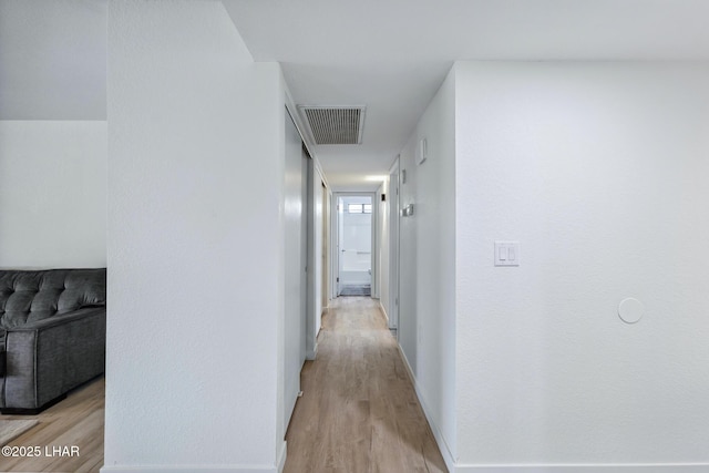 corridor with baseboards, visible vents, and light wood-style floors