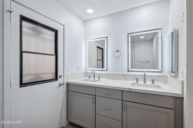 full bathroom with a textured wall, double vanity, a textured ceiling, and a sink