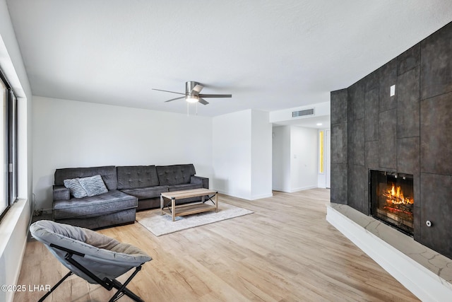 living room with visible vents, light wood-style floors, ceiling fan, a tile fireplace, and baseboards