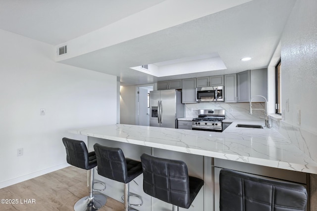 kitchen featuring light stone countertops, gray cabinetry, stainless steel appliances, a sink, and decorative backsplash