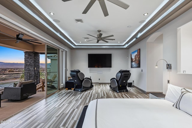 bedroom with access to exterior, visible vents, wood finished floors, arched walkways, and a raised ceiling