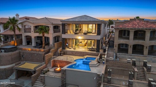 back of house at dusk with a tile roof, stucco siding, a balcony, an outdoor pool, and a patio