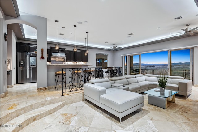 living area with arched walkways, visible vents, a tray ceiling, and ceiling fan