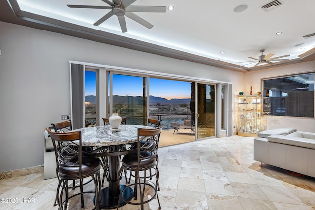 dining area featuring visible vents, ceiling fan, a tray ceiling, stone tile flooring, and a mountain view