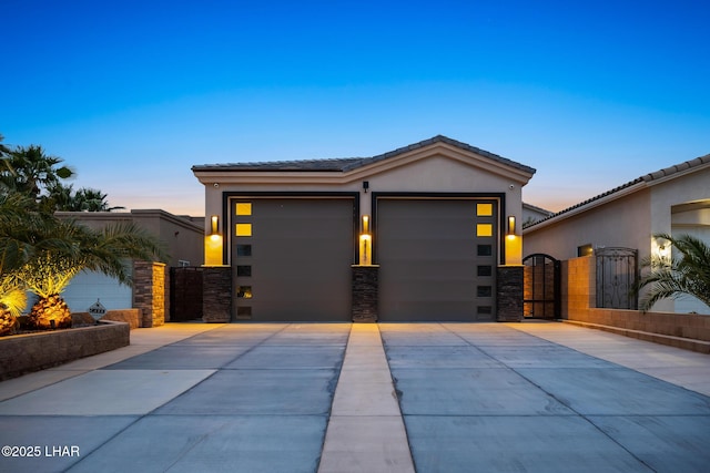 view of front of house featuring an attached garage, a tile roof, stucco siding, driveway, and a gate