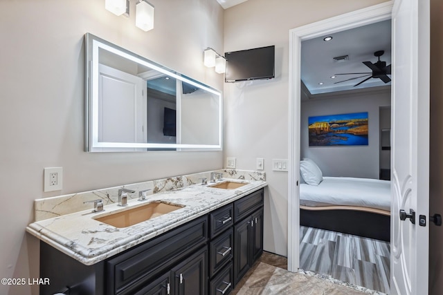 ensuite bathroom with a sink, visible vents, ceiling fan, and double vanity