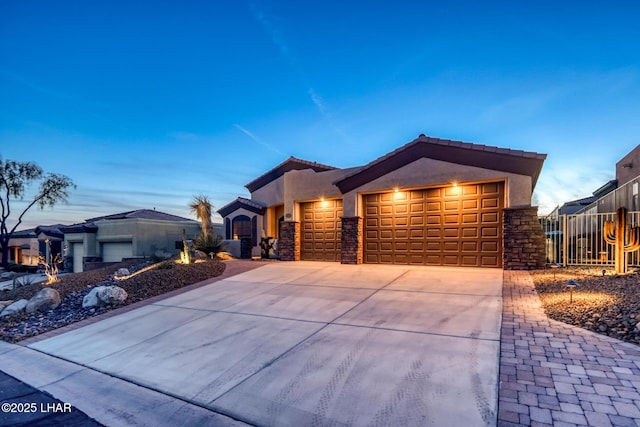 view of front of property featuring stucco siding, driveway, a tile roof, stone siding, and a garage