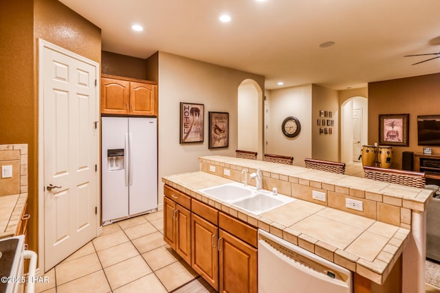 kitchen with a sink, open floor plan, tile countertops, white appliances, and arched walkways