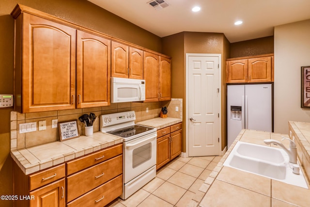 kitchen with white appliances, light tile patterned floors, visible vents, a sink, and backsplash