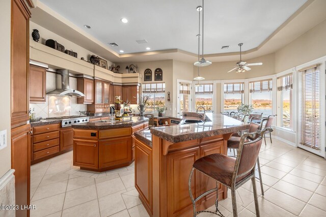 8480 Miraleste Shores Dr, Parker, AZ 85344 - kitchen with wall chimney exhaust hood, a kitchen island with sink, stainless steel gas cooktop, brown cabinetry, and light tile patterned floors