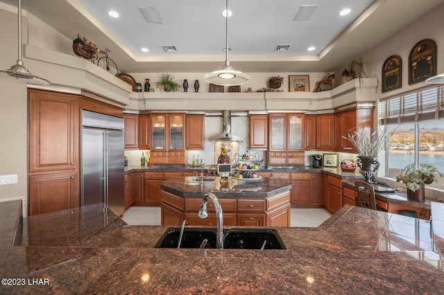 8480 Miraleste Shores Dr, Parker, AZ 85344 - kitchen with built in refrigerator, wall chimney exhaust hood, brown cabinets, a tray ceiling, and a towering ceiling