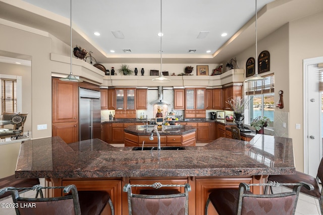 8480 Miraleste Shores Dr, Parker, AZ 85344 - kitchen with stainless steel built in fridge, brown cabinetry, a kitchen island with sink, a kitchen breakfast bar, and wall chimney exhaust hood