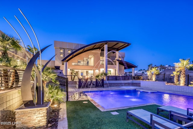 pool at dusk featuring pool water feature, a yard, a hot tub, and a patio