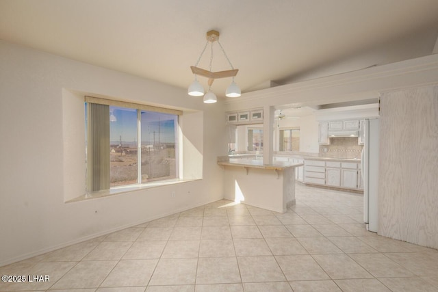 kitchen with light tile patterned floors, a kitchen breakfast bar, white cabinets, decorative light fixtures, and kitchen peninsula