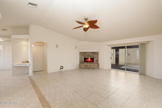 unfurnished living room with vaulted ceiling, a stone fireplace, light tile patterned floors, and ceiling fan