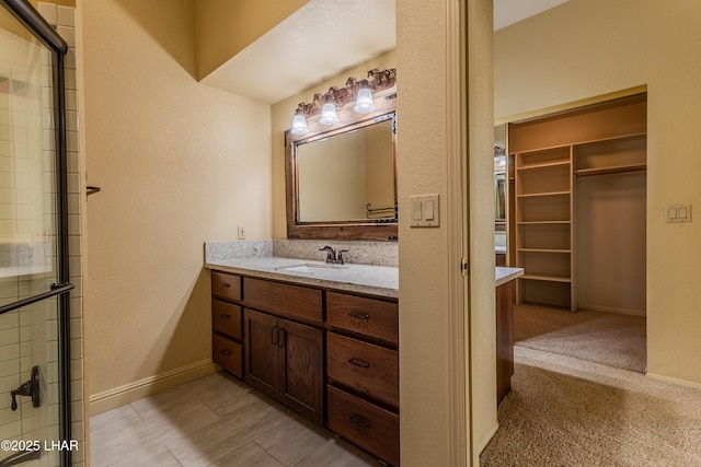 bathroom featuring a tile shower, a spacious closet, vanity, and baseboards