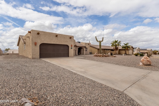 pueblo-style home featuring stucco siding, driveway, a garage, and fence