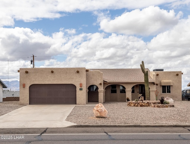 pueblo revival-style home with an attached garage, driveway, and stucco siding